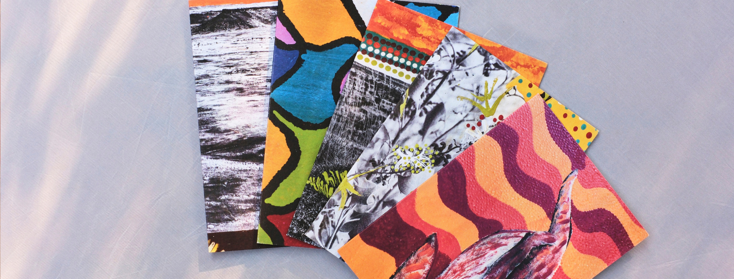 A fan of small, colourful art cards arranged in a loose stack on a light fabric surface. Each card features bold, abstract patterns and textures in warm tones.